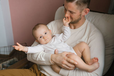 A happy contented father holds his baby son in his arms and sits at home in an armchair