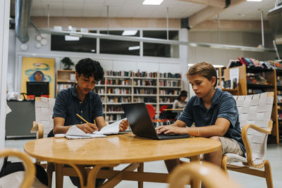 Focused male students studying while sitting near table in library at junior high school