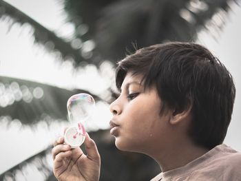 Close-up of boy blowing bubble against palm tree
