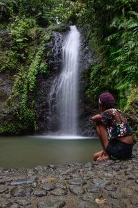 Woman sitting on rock looking at waterfall