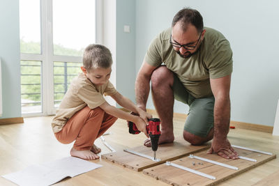 Father with son using drill on plank at home