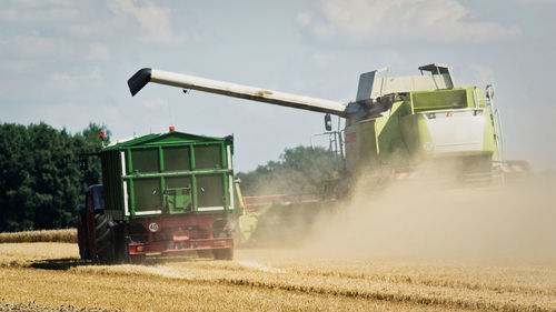 Combine harvester with tractor on agricultural field against sky