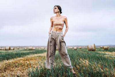 Smiling woman in sunglasses with bare shoulders on a background of wheat field and bales of hay.