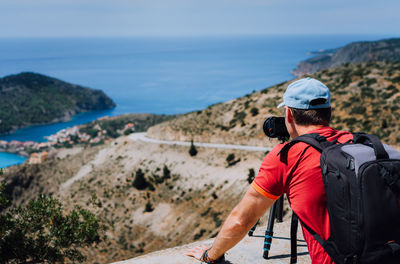 Rear view of backpacker photographing on mountain against sky during sunny day