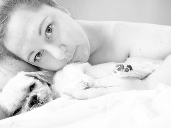 Portrait of young woman with dog lying down on bed at home