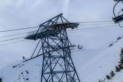 Low angle view of electricity pylon against sky during winter