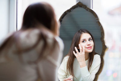 Rear view of woman applying make-up while looking at mirror