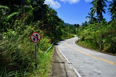 Road sign by trees against sky