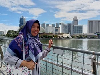 Portrait of smiling young woman standing against city