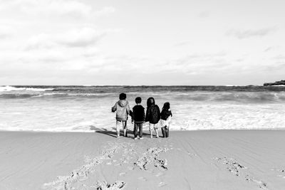 Rear view of friends standing at beach against sky