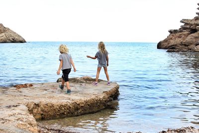 Siblings at beach against sky