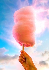 Low angle view of hand holding cotton candy against sky