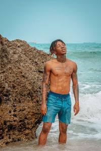 Full length of shirtless man standing at beach against sky