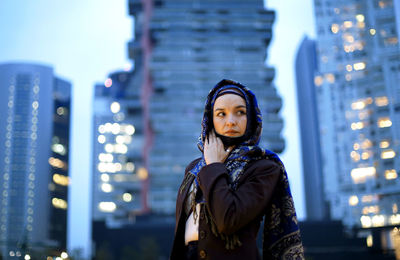 Portrait of young woman standing against illuminated city at night