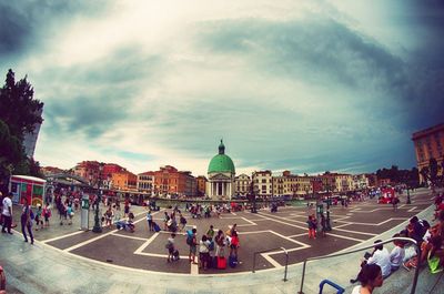 People walking in front of building against cloudy sky