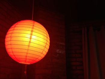 Low angle view of illuminated lantern against brick wall
