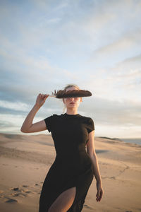 Rear view of woman standing at beach against sky during sunset