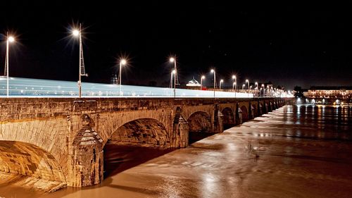 Illuminated bridge over river against sky at night