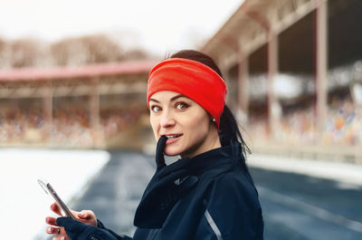 Pretty fitness girl runner in red bandana on winter stadium looking at camera