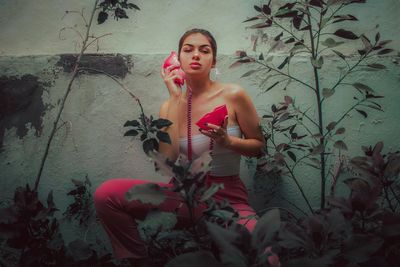 Portrait of young woman holding artificial telephone against wall