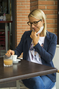 Woman at a café's table pulling down her mask to be able to drink a coffee. 