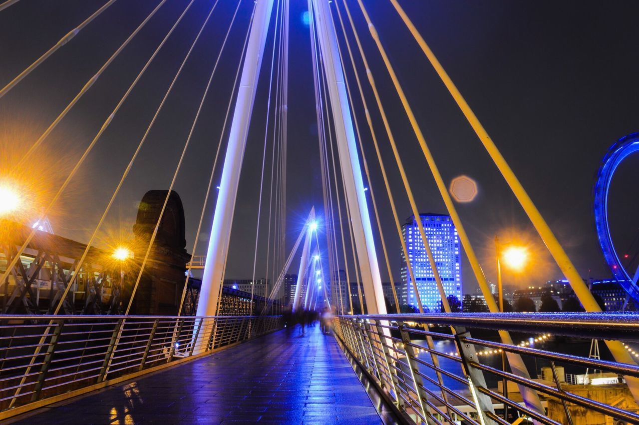 illuminated, night, built structure, architecture, bridge - man made structure, city, connection, building exterior, modern, engineering, water, transportation, suspension bridge, river, sky, long exposure, blue, skyscraper, street light, reflection