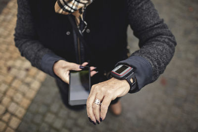 Low section of woman using phone while checking the time on footpath