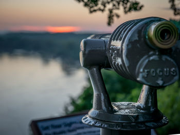 Coin-operated binoculars by lake against sky during sunset