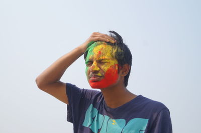 Man with powder paint on face standing against clear sky during holi