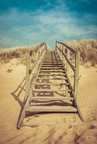 Surface level of boardwalk on beach against sky