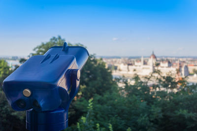 Coin-operated binoculars in city against sky