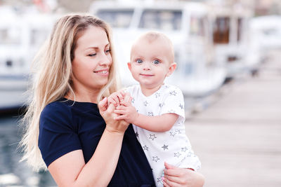 Smiling woman holding baby boy 1 year old over sea background. looking at camera. motherhood.