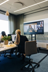 Male and female colleagues doing video call with businesswoman on tv in coworking office