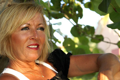 Close-up of smiling mature woman looking away while standing against tree