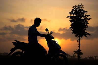 Silhouette people riding motorcycle against sky during sunset