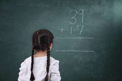 Rear view of girl learning mathematics on blackboard