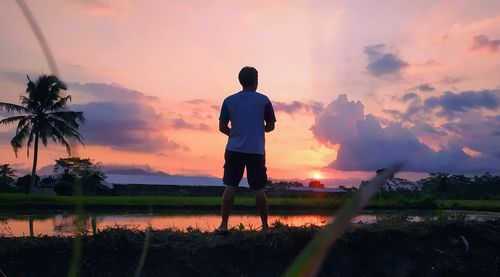 Rear view of silhouette man standing on field against sky during sunset