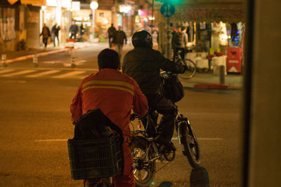 Rear view of people riding bicycle on road at night