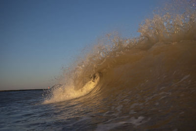 Waves splashing in sea against clear sky at sunset