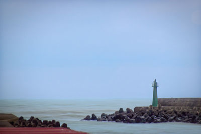 Lighthouse by sea against clear blue sky