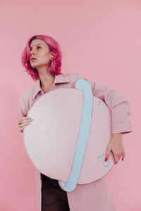 Beautiful young woman holding artificial saturn while standing against colored background