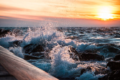 Waves splashing on sea against sky during sunset