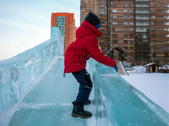 Unrecognizable eight-year-old boy in the city standing in sideways on an ice slide.