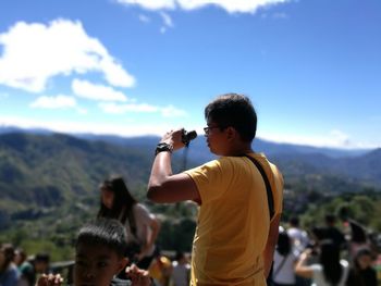 Side view of man looking through binoculars while standing against mountains