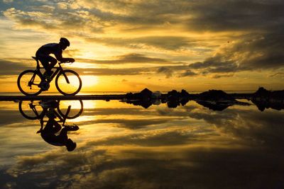 Silhouette man cycling at beach against sky during sunset