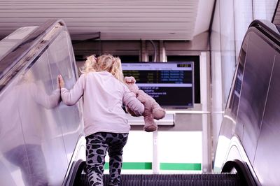 Rear view of girl standing on escalator