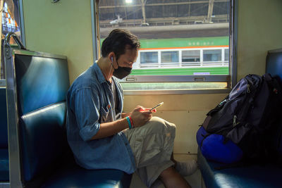 An asian man wearing casual wear a face mask using a cell phone in a train at the train station