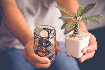 High angle view of woman holding jar of coins and potted plant