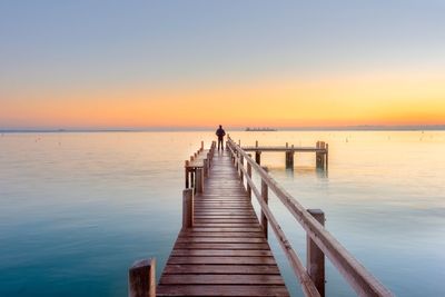 Rear view of person standing on pier against clear sky during sunset