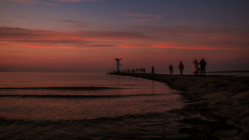 Silhouette people on beach against sky during sunset